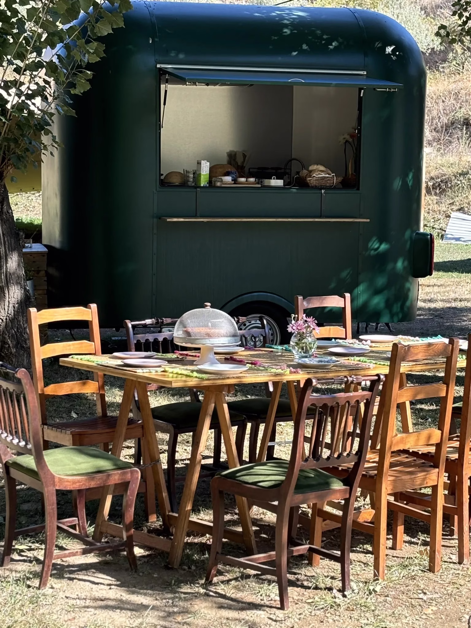 Mesa rústica ao ar livre com cadeiras de madeira e foodtruck verde ao fundo na Quinta da Ponte